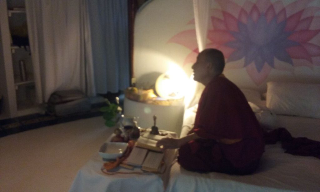 Monje budista sentado en meditación junto a una ventana con luz natural.