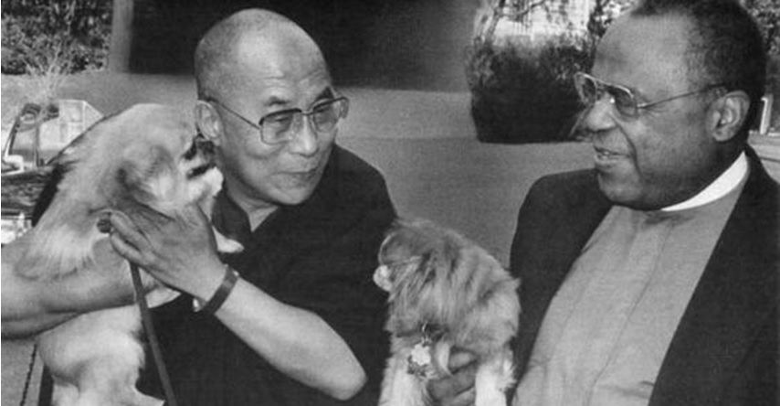 Fotografía en blanco y negro del Dalai Lama acariciando a un perro pequeño.