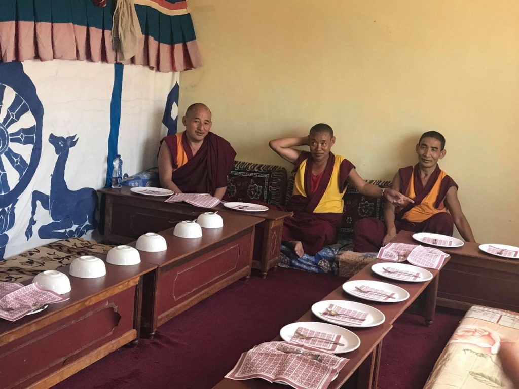 Varios monjes budistas sentados en fila con cuencos de ofrenda.