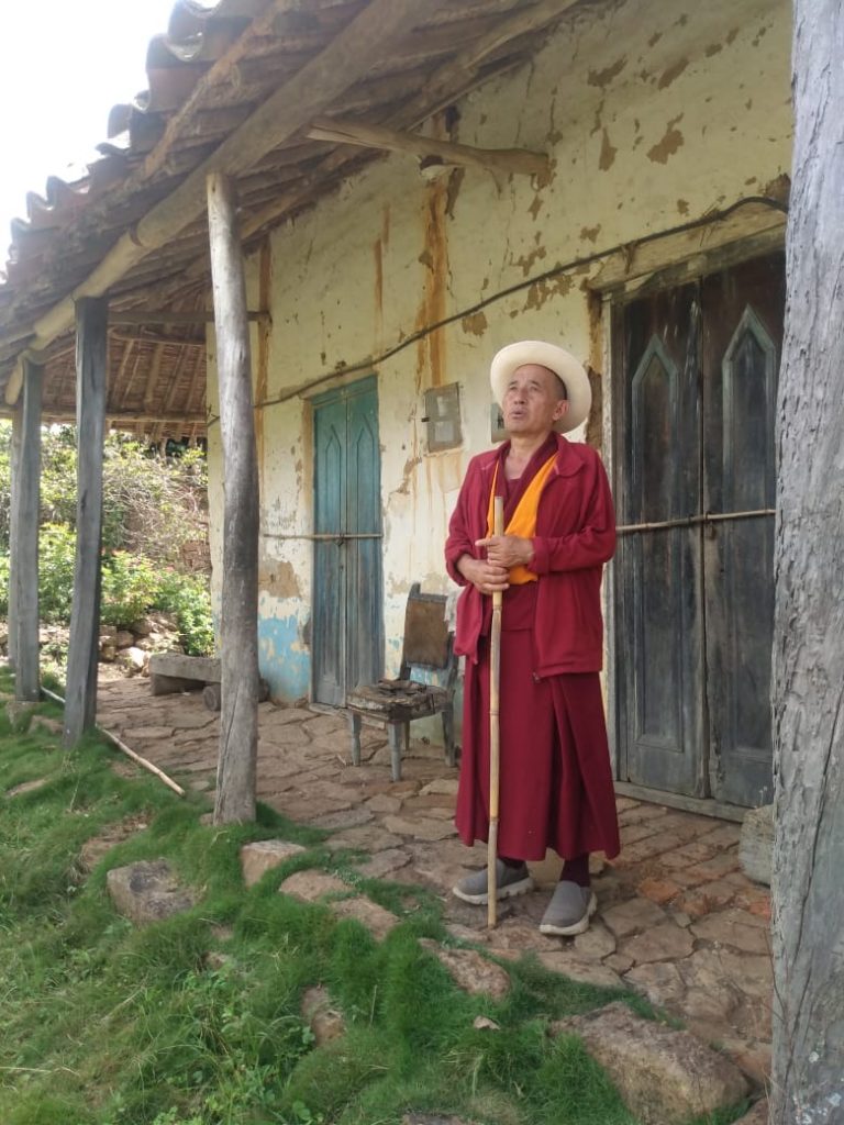 Monje budista junto a una casa rural de paredes de tierra.