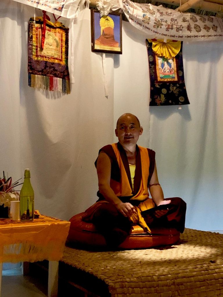 Monje budista meditando sentado en una sala con thangkas colgados.