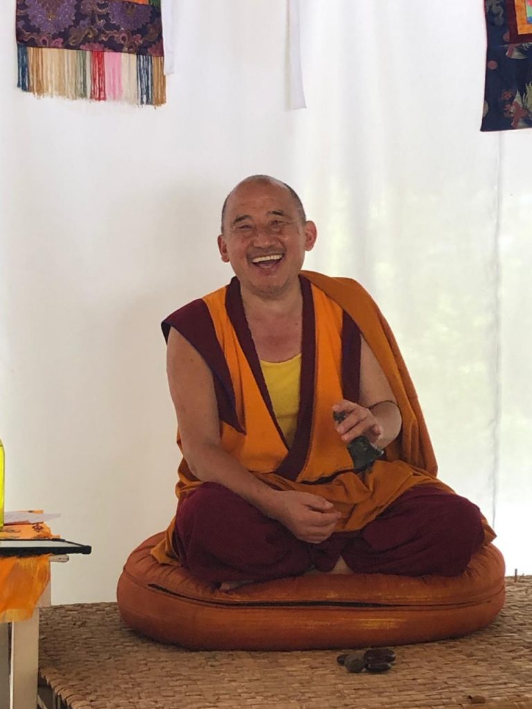 Monje budista sentado y sonriendo sobre un cojín de meditación.