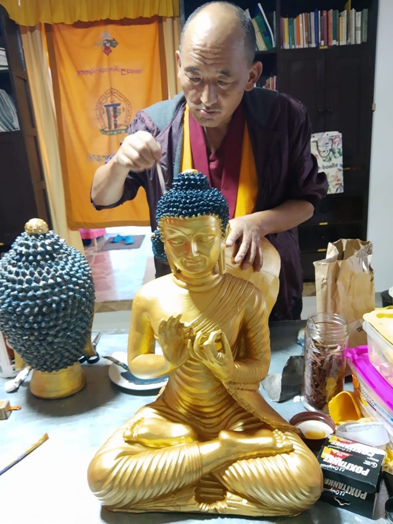 Monje budista pintando una escultura dorada.