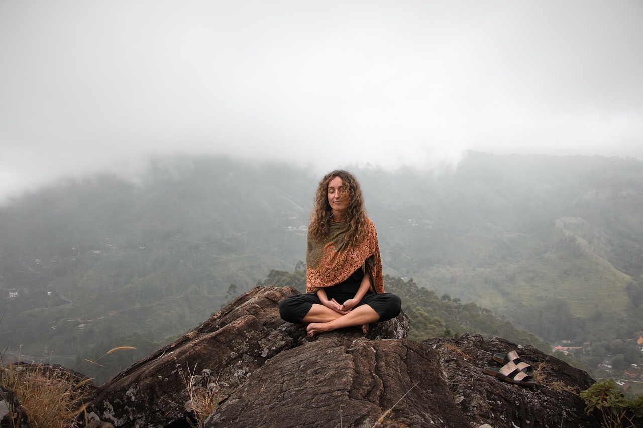 Mujer meditando sobre una roca frente a un paisaje de montaña.