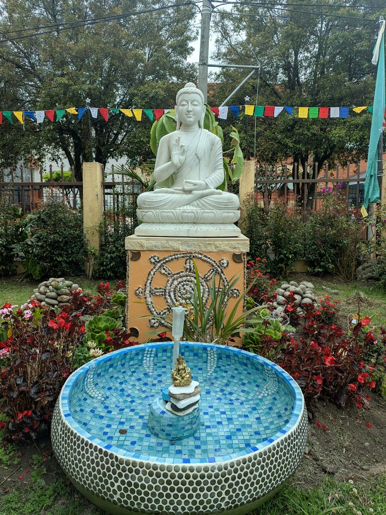 El jardín de la sede del Centro Yamantaka, con el Buda blanco sobre su pedestal, la fuente de mosaico azul y las banderas de oración.