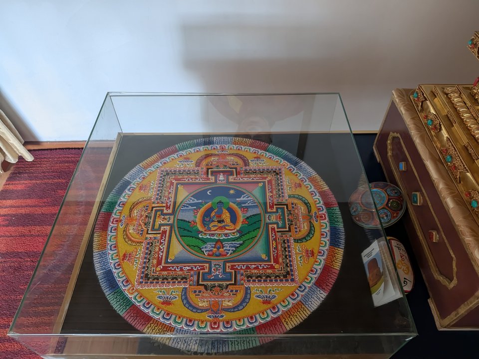 Mandala de arena del Buda de la Medicina en su vitrina, con la deidad central azul y el palacio de cuatro puertas.